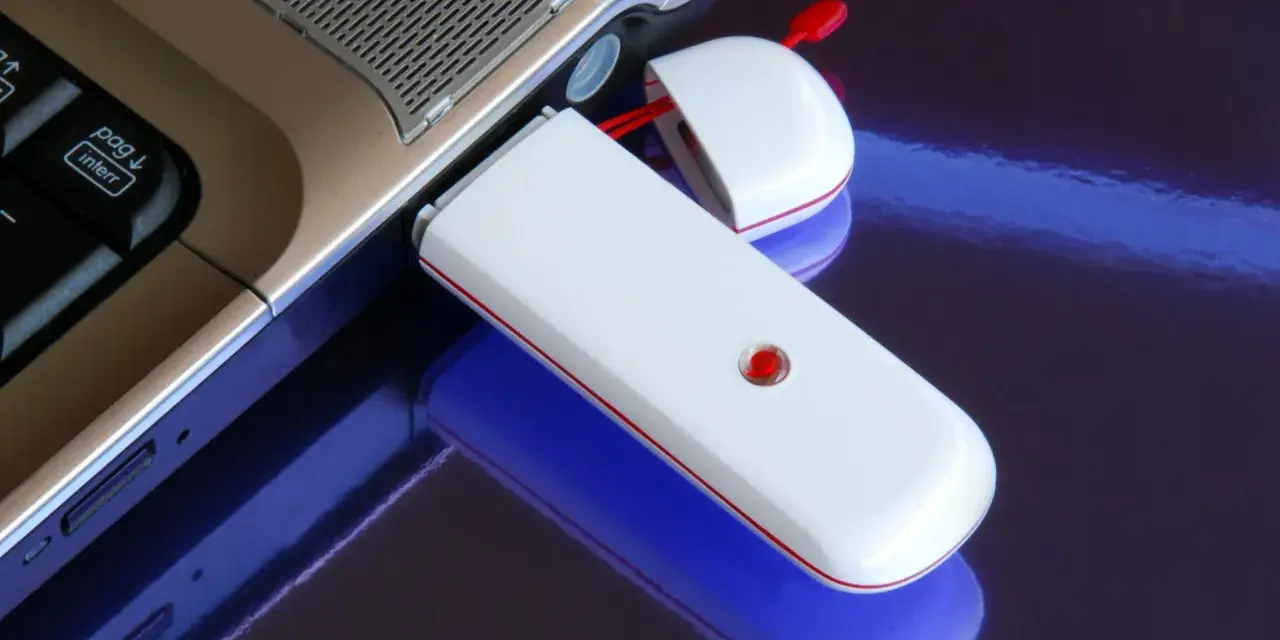 Biały modem USB podłączony do laptopa, umożliwiający komórkową transmisję danych.