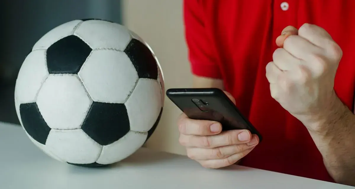 Piłka nożna i smartfon. Kibic sprawdza wynik, licząc na powyżej 2.5 gola.