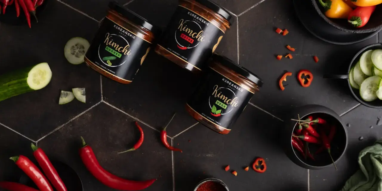 Słoiki z kimchi, papryczki chili, ogórek i przyprawy na czarnym tle.