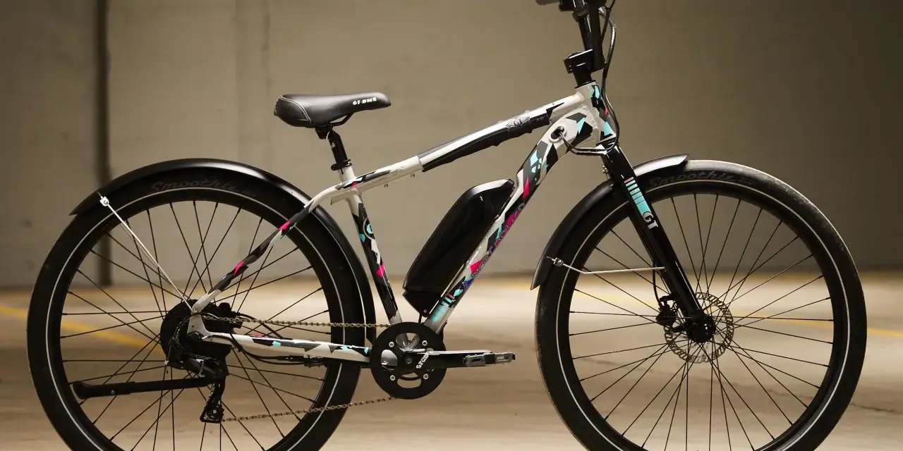 A white GT power performer electric bike with a colorful geometric pattern, parked indoors.