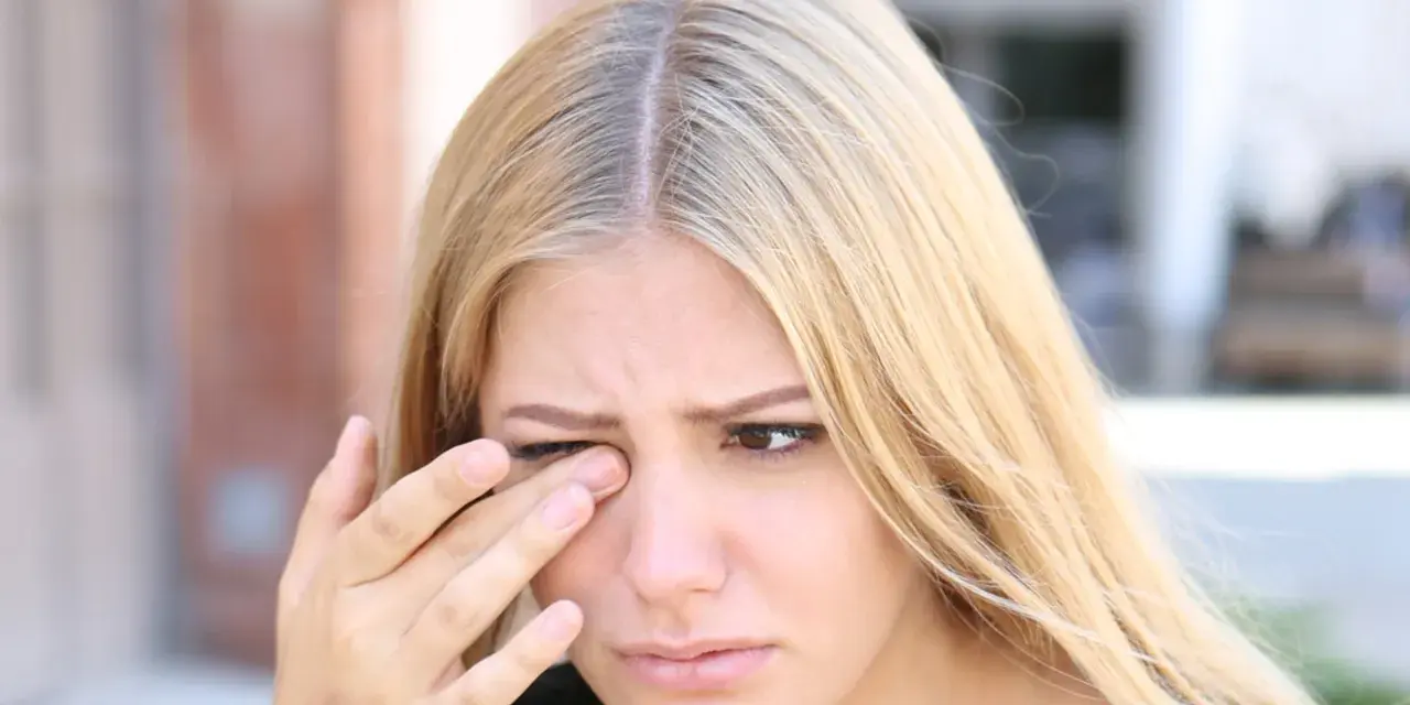 Kobieta z blond włosami pociera oko, co może być jednym z objawów niedoboru witaminy B.