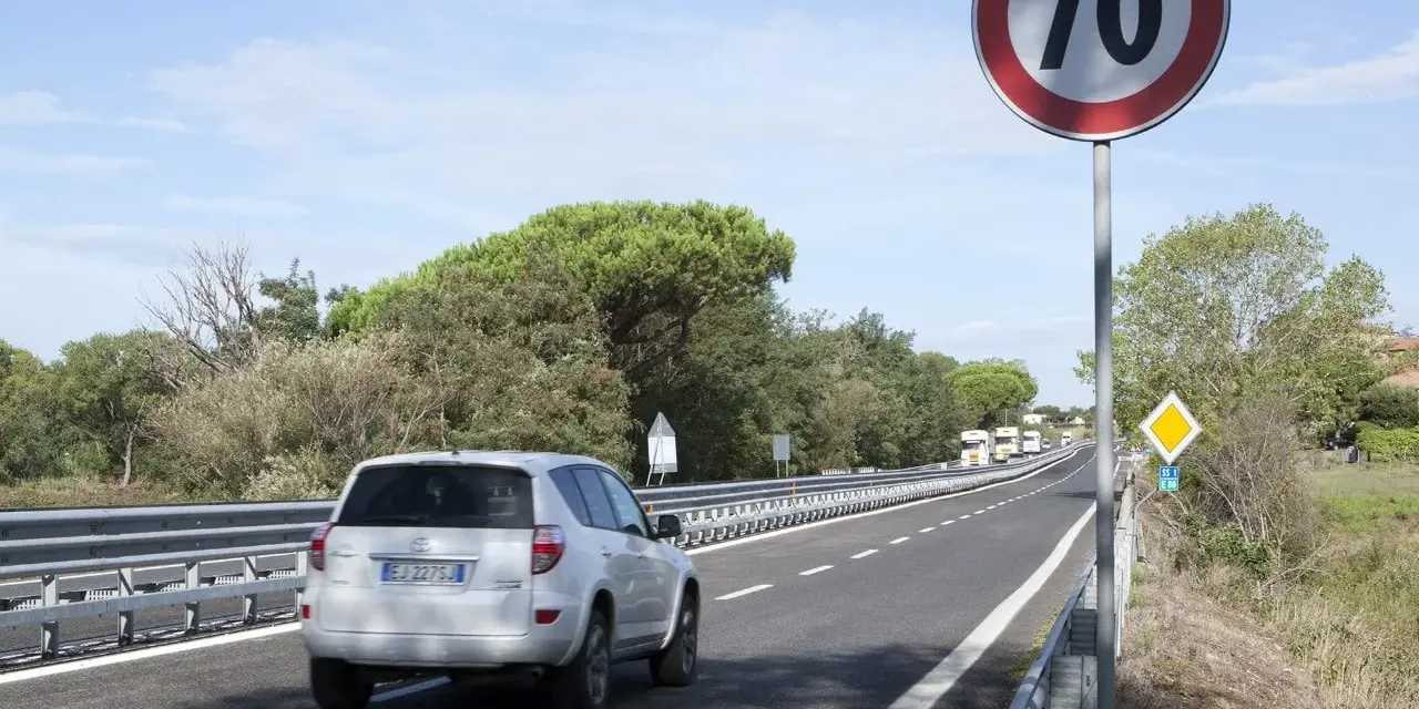 Un'auto bianca percorre una strada extraurbana secondaria, superando un cartello di limite di velocità a 70 km/h.