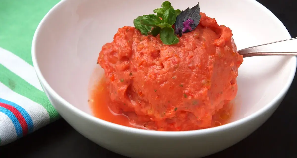 Ein erfrischendes Tomaten-Eis, garniert mit Basilikum, in einer weißen Schüssel.