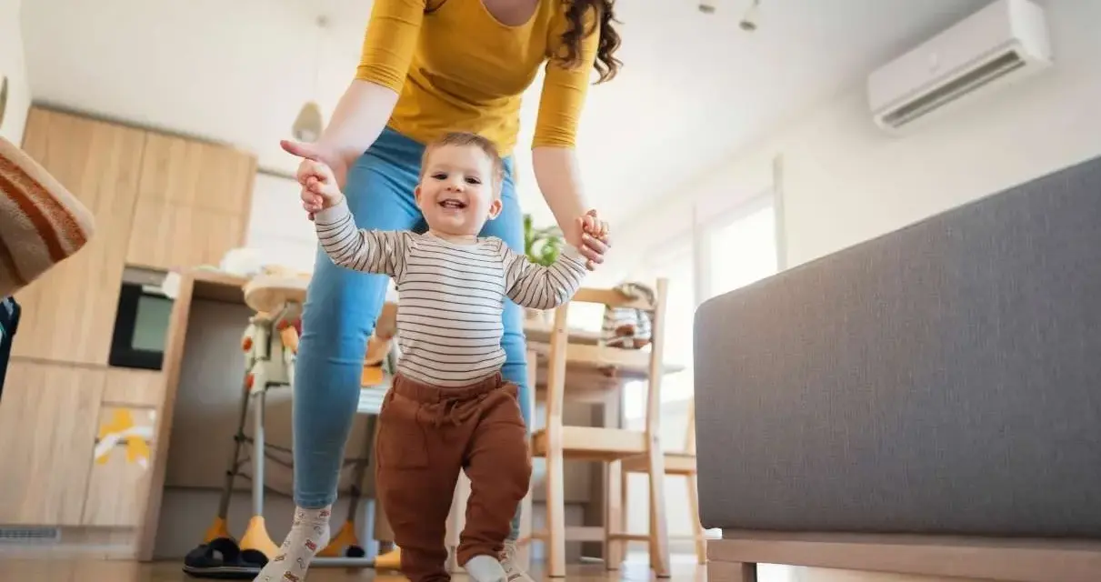 Mamá ayuda a su bebé a dar sus primeros pasos en una habitación cómoda, con el aire acondicionado bebes funcionando para mantener la temperatura ideal.