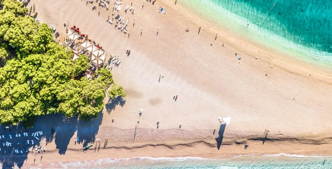 Chorwacja plaże piaszczyste, z turkusową wodą i zielonymi drzewami. Leżaki i parasole czekają na plażowiczów.