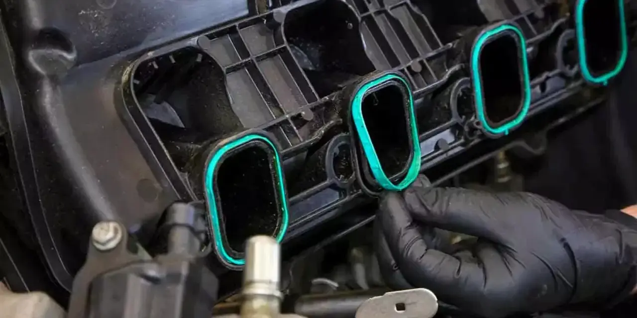 A gloved hand installs a new intake manifold gasket, ensuring a tight seal for optimal engine performance.