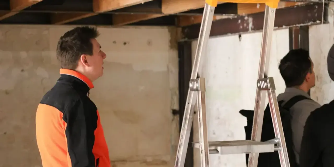 Un homme en veste orange et noire observe le plafond délabré d'un chantier. L'architecte assure le suivi de chantier, une obligation pour garantir la qualité des travaux.