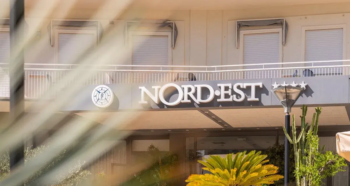 Hotel Nord Est sign with a compass logo and five stars, framed by palm fronds.