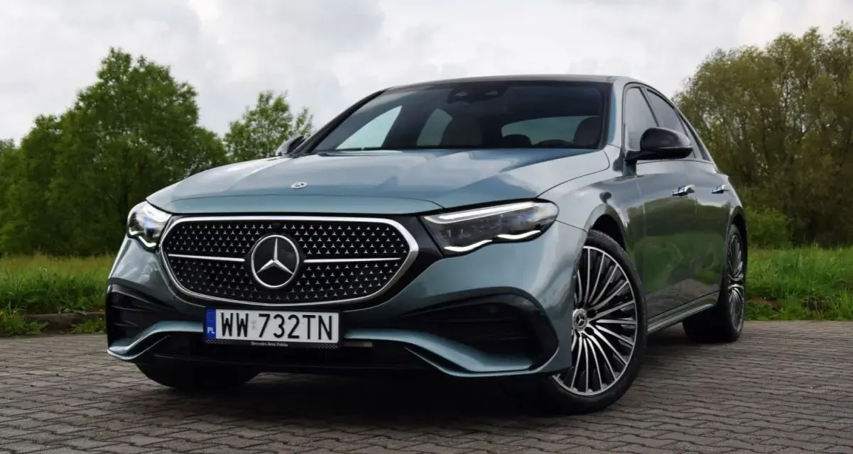 Elegancki Mercedes E220d w kolorze miętowym, zaparkowany na brukowanej nawierzchni, z zielenią w tle.