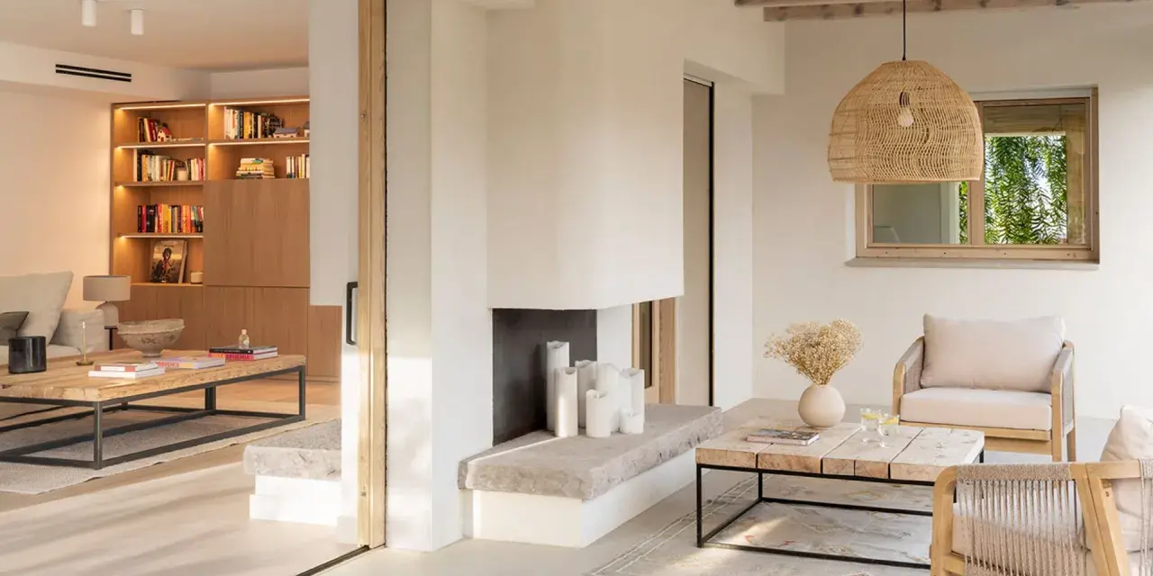 Salón luminoso con chimenea de piedra, muebles de madera y textiles naturales, evocando un relajante estilo ibicenco.