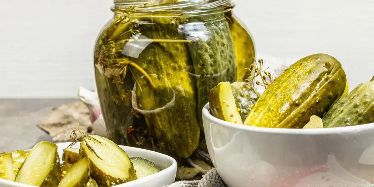 Cetrioli in agrodolce in un barattolo di vetro e in ciotole, con aglio e spezie.