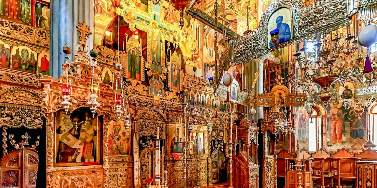 Interior of a richly decorated Orthodox church, showcasing ornate iconostasis, frescoes, and chandeliers, typical of many ancient christian monasteries.