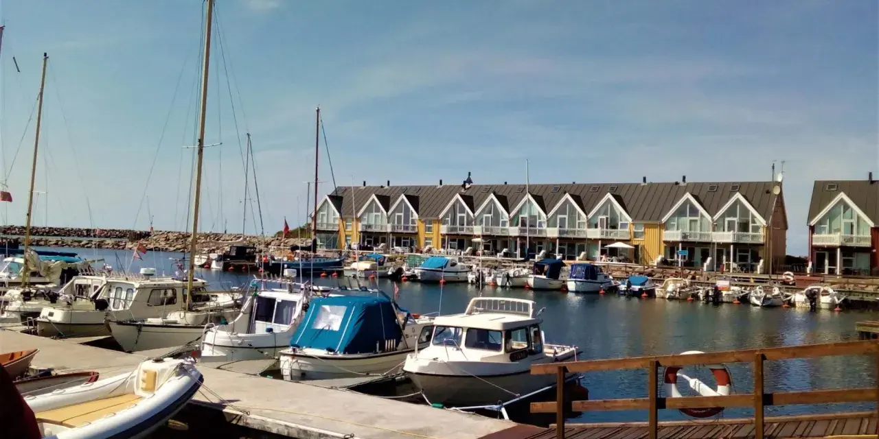 Port z łodziami i domkami w tle. Planujesz podróż rowerem na Bornholm? Koszty mogą być różne, ale widok jest wart każdej ceny.