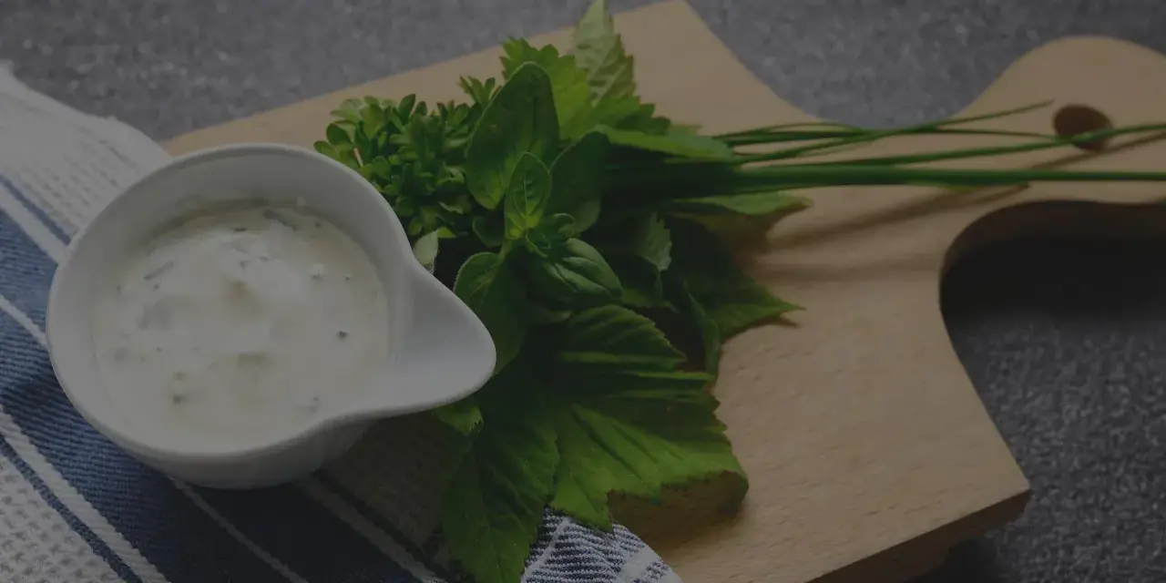 Sauce tartare maison crémeuse dans un ramequin blanc, accompagnée d'herbes fraîches sur une planche en bois.