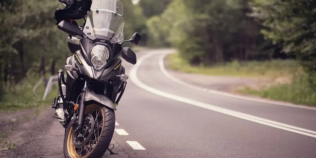 Moto pronta per avventurosi itinerari in moto su una strada tortuosa tra alberi. Casco appoggiato sul manubrio.