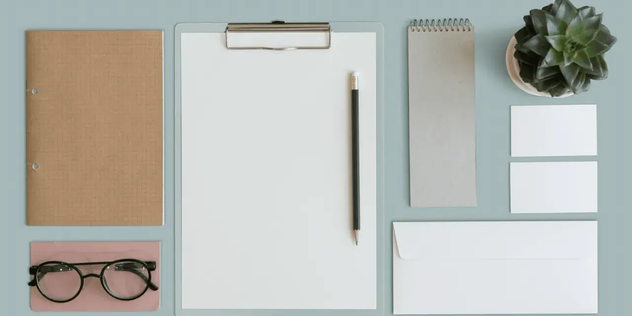 Un bureau minimaliste avec un carnet, des lunettes, un presse-papiers, un crayon, un carnet, une plante et des cartes de visite. Un exemple de book artistique.