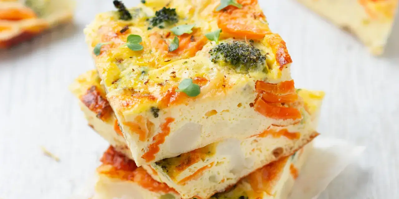 Fette di frittata al forno con verdure, broccoli e carote, guarnita con germogli freschi. Un piatto colorato e salutare.