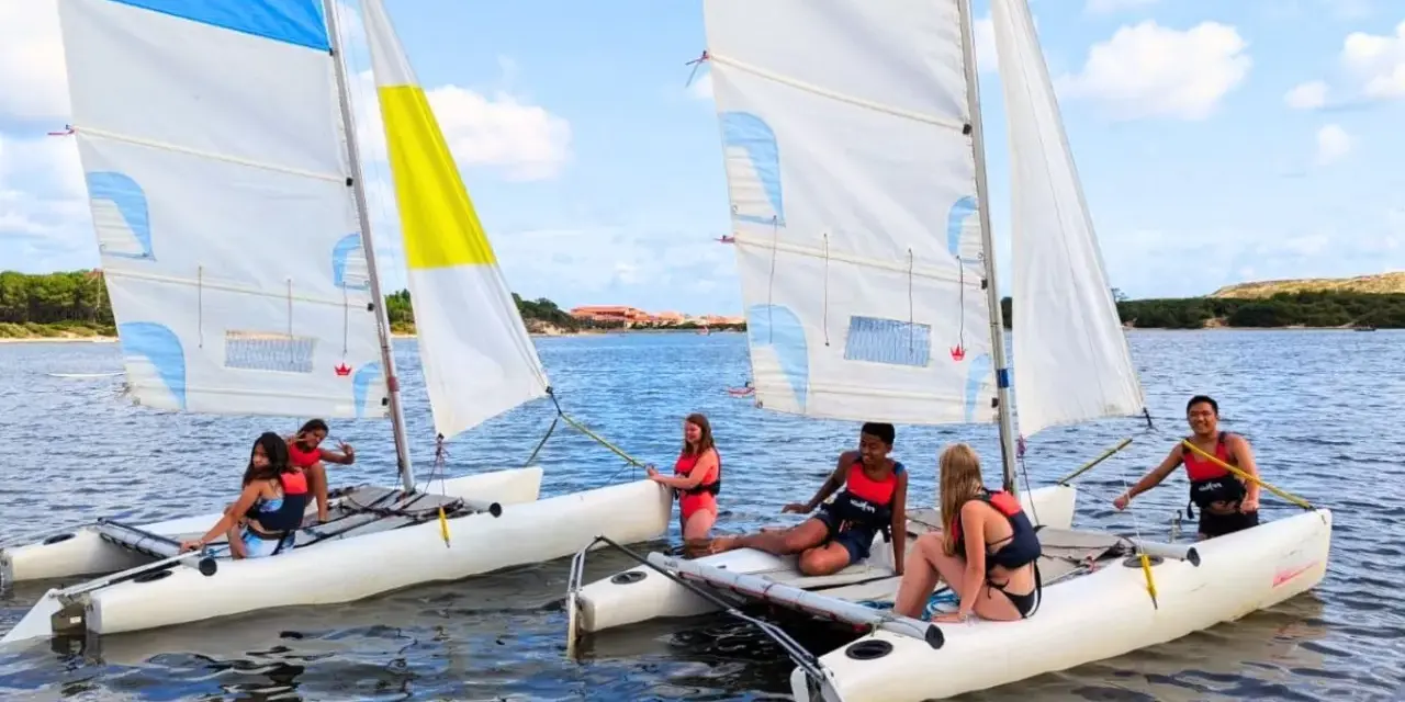 Des jeunes profitent d'une colonie de vacances voile, naviguant sur des catamarans par une journée ensoleillée.
