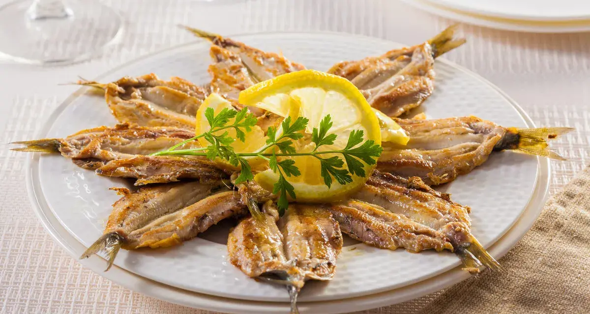 Piatto di alici alla scapece disposte a raggiera, guarnite con fette di limone e prezzemolo.