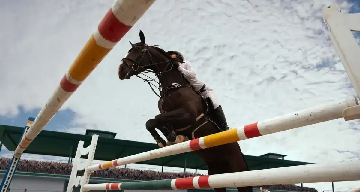 Un cheval brun et son cavalier en blanc effectuent un spectaculaire saut d'obstacles, le tout sous un ciel nuageux.