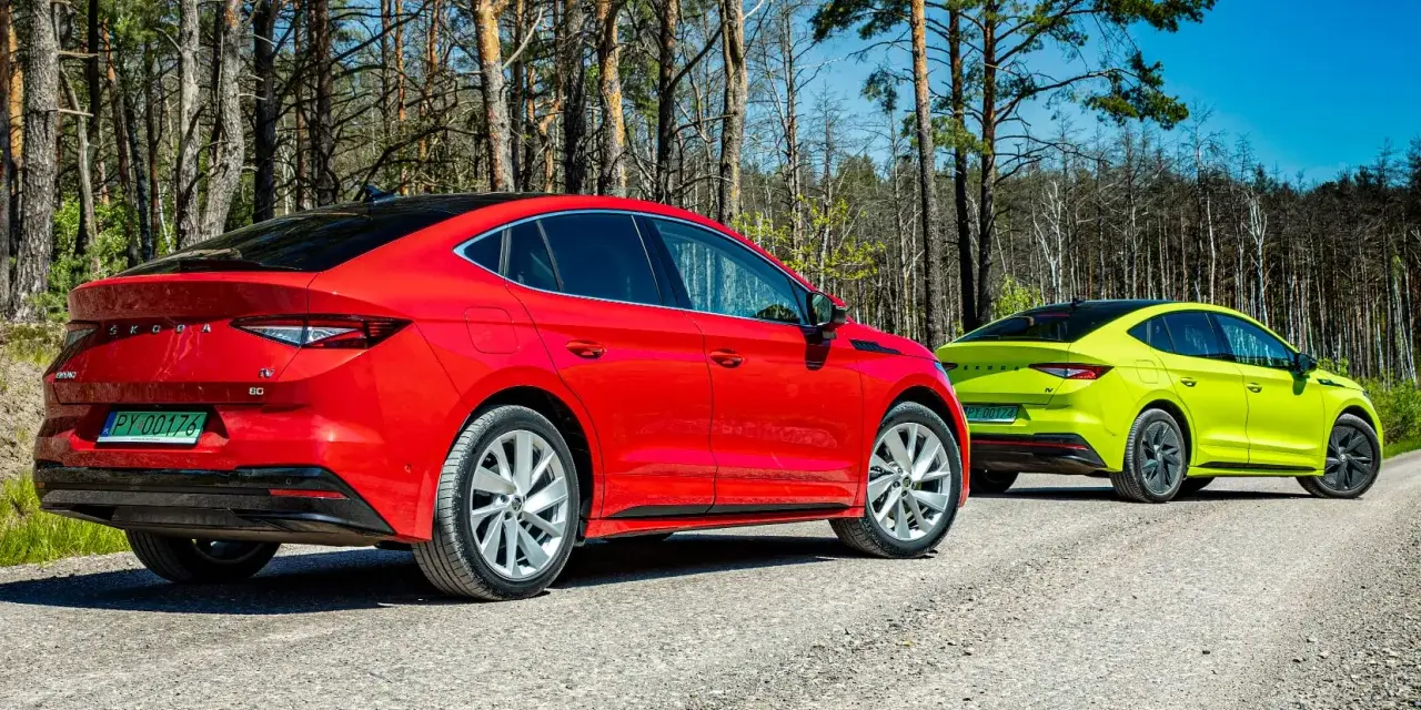 Dwa samochody Skoda Enyaq w kolorach czerwonym i limonkowym na leśnej drodze.