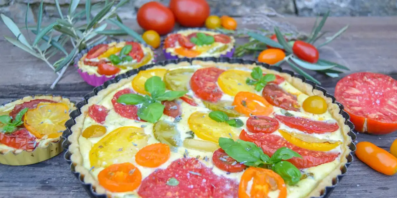 Eine herzhafte Tomaten Quiche mit bunten Tomatenscheiben und frischem Basilikum, garniert mit Lavendelblüten.