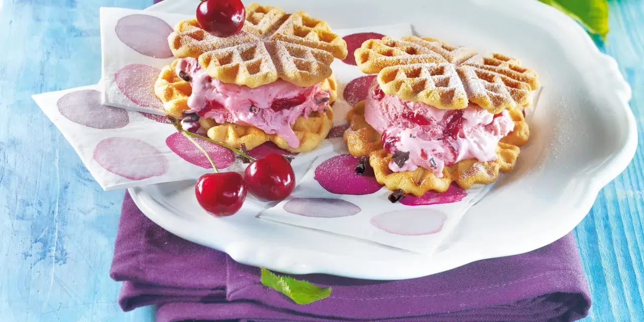 Zwei herzförmige Waffeln gefüllt mit Kirscheis und Schokostückchen, garniert mit frischen Kirschen. Ein süßer Genuss!