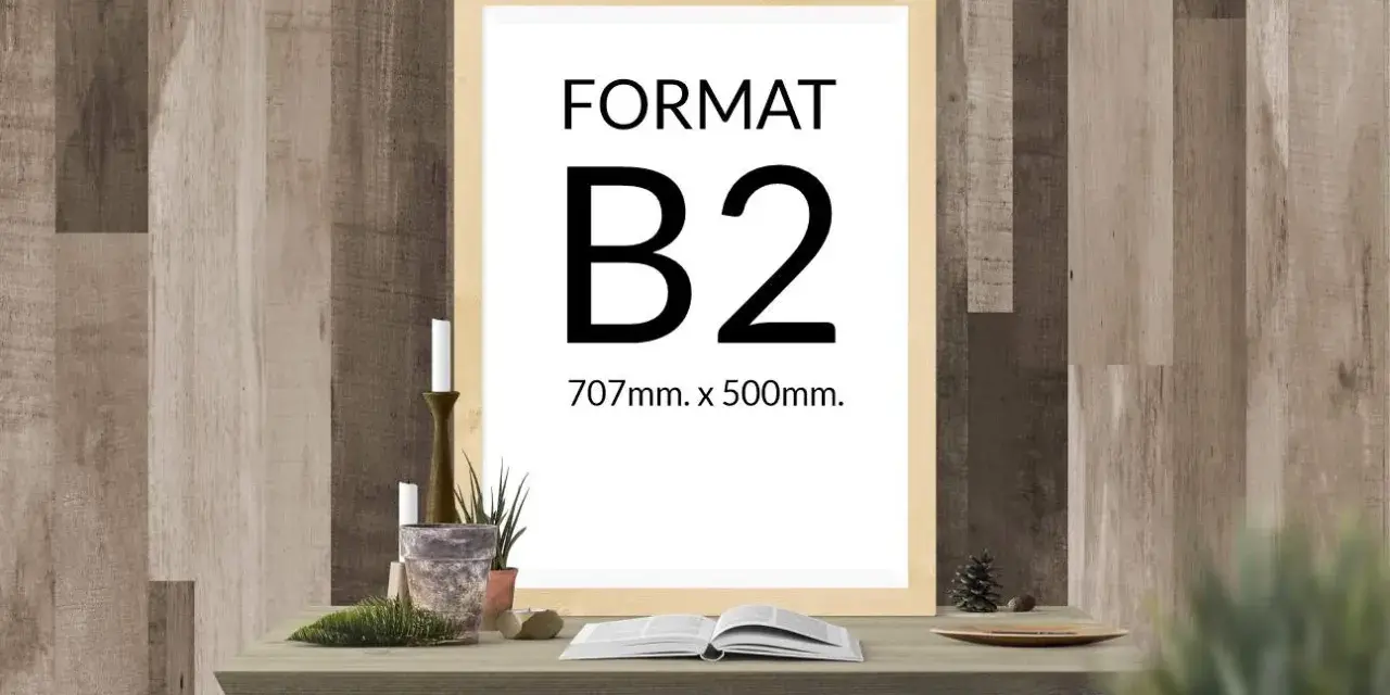 Ramka z napisem "FORMAT B2 707mm. x 500mm." na tle drewnianej ściany. Na stole obok książka i świece.