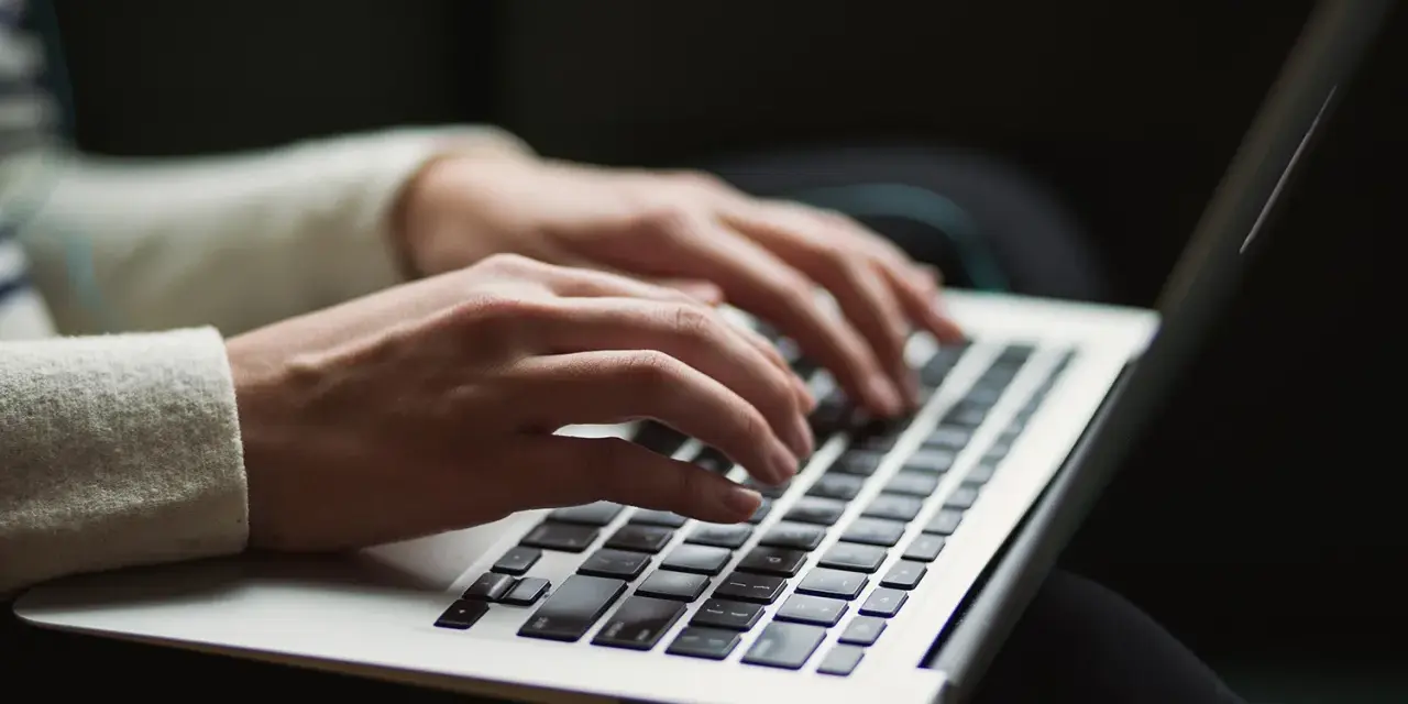 Dłonie piszą na laptopie. Ktoś przygotowuje wypowiedzenie umowy o pracę po angielsku, szukając wzoru.