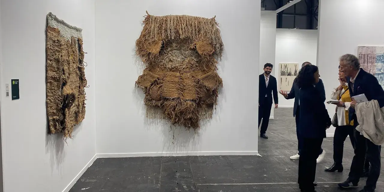 Exposición de arte contemporáneo con tapices texturizados y personas observando.