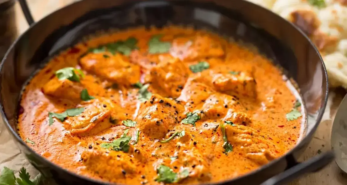 Aksamitny kurczak w sosie curry, udekorowany świeżą kolendrą, kusi aromatem. Obok widać kawałki chleba naan.