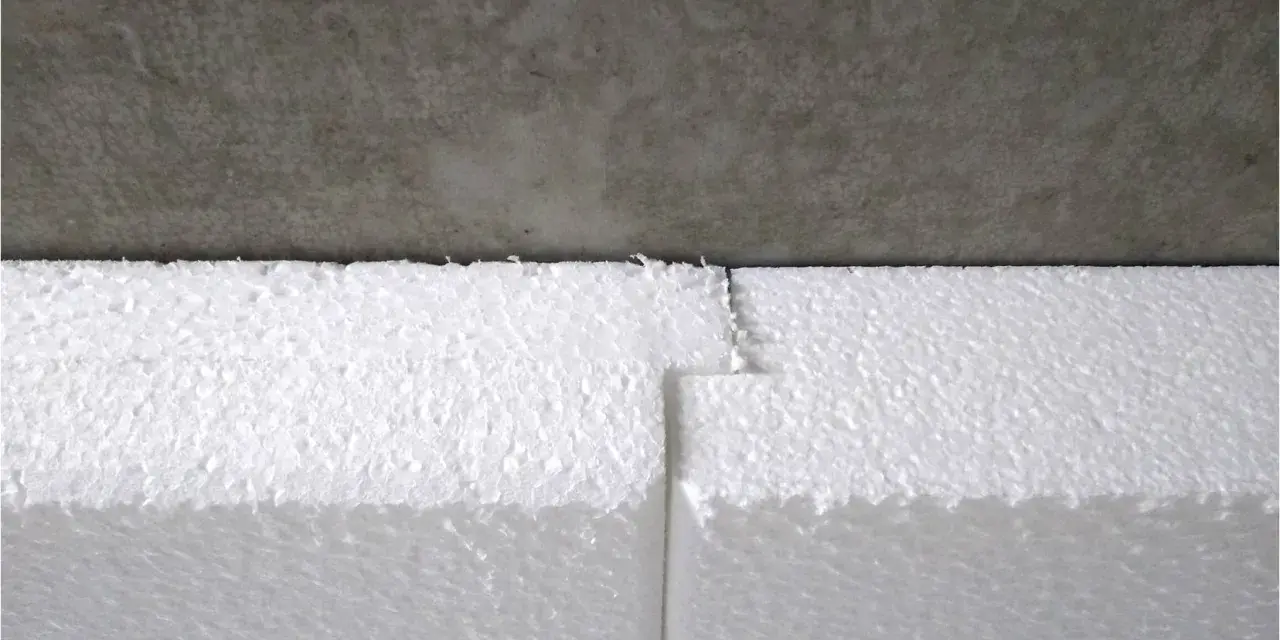 Detailaufnahme: Styrodur kleben an einer Betonwand. Die weißen Styroporplatten sind präzise zugeschnitten und stoßen nahtlos aneinander.