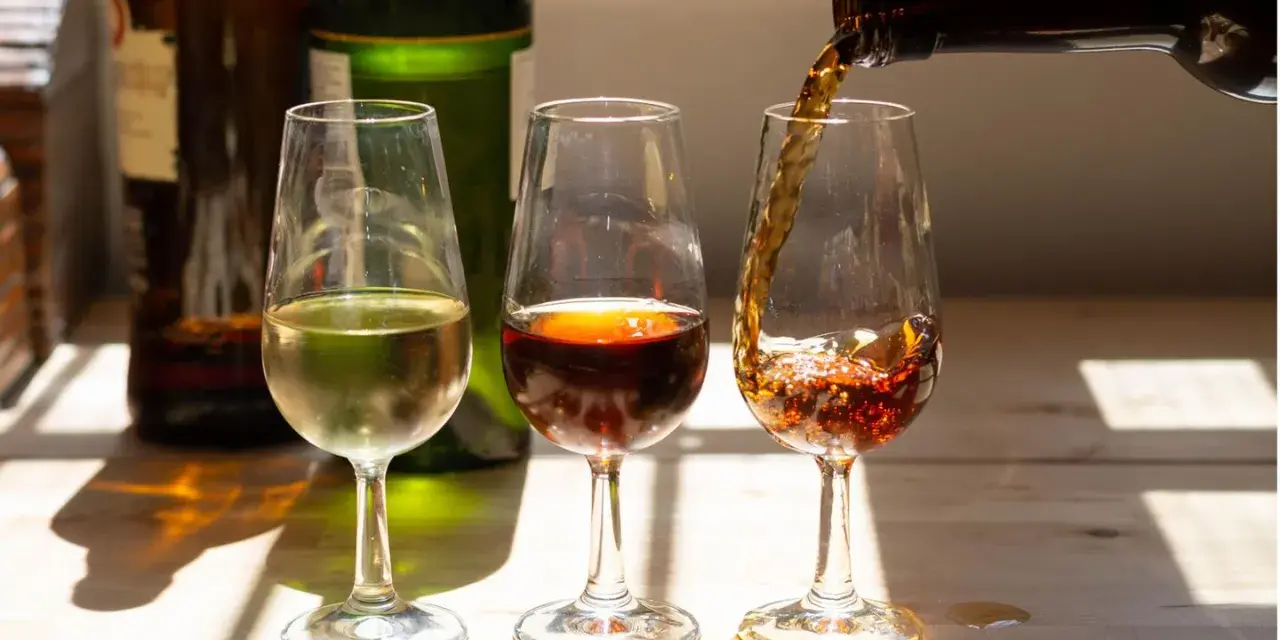 Drei Gläser mit Sherry-Alkohol: ein helles, ein dunkles und ein drittes, in das gerade eingeschenkt wird.