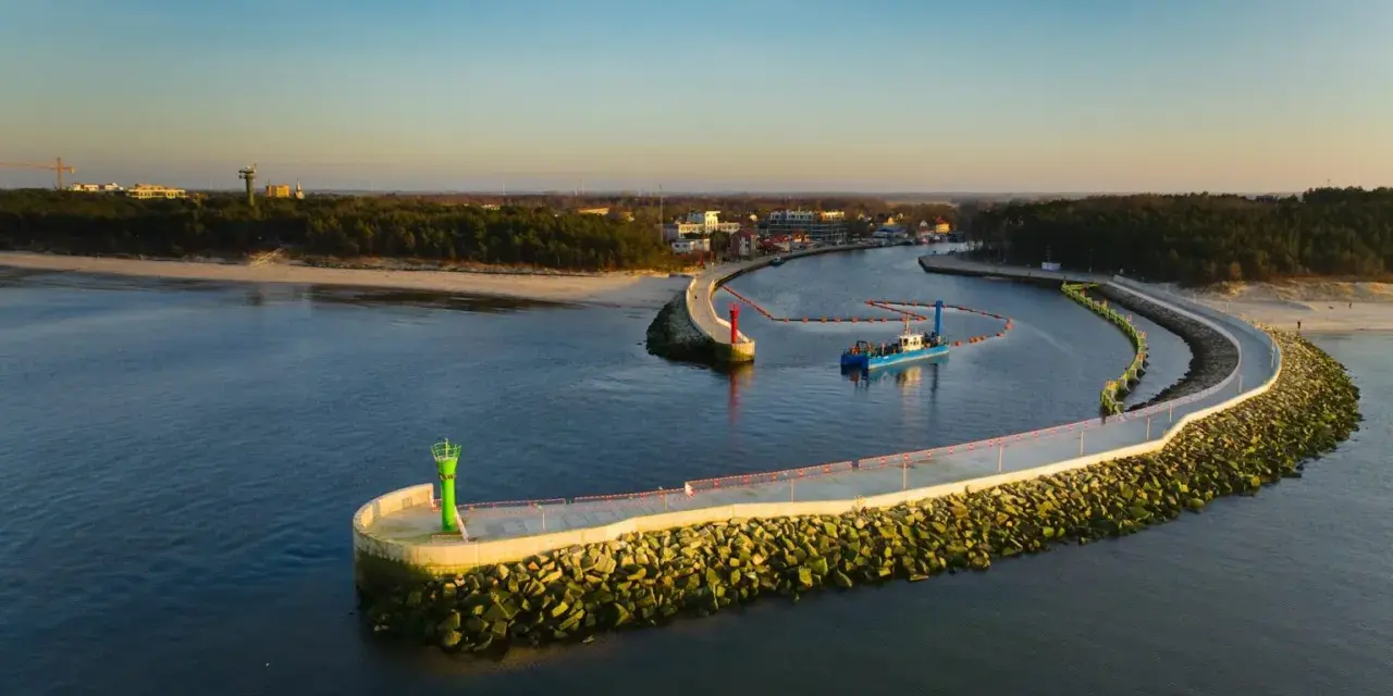 Port w Mrzeżynie z falochronami i latarniami morskimi. Widoczna łódź pogłębiarka. Mrzeżyno atrakcje dla miłośników morza.