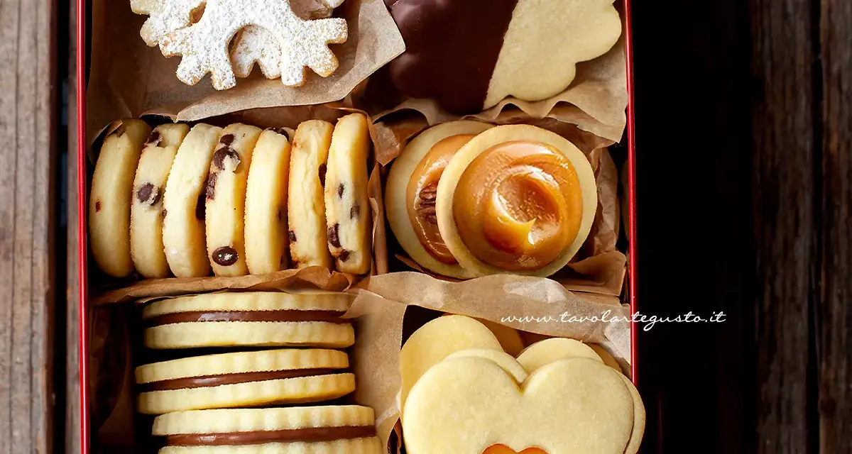 Scatola piena di biscotti al burro: fiocchi di neve, con gocce di cioccolato, ripieni di caramello e a forma di cuore.