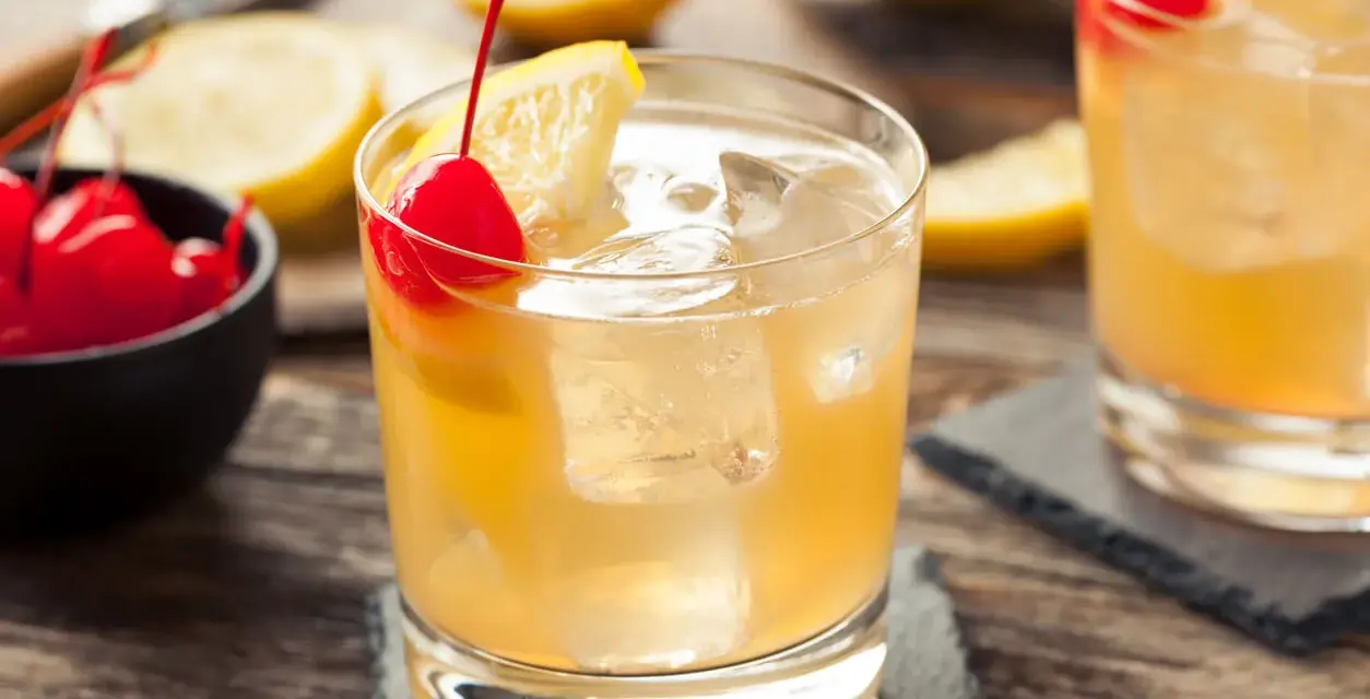 En gyllene whiskey sour med is, citron och körsbär. En klassisk drink som passar perfekt en varm dag.