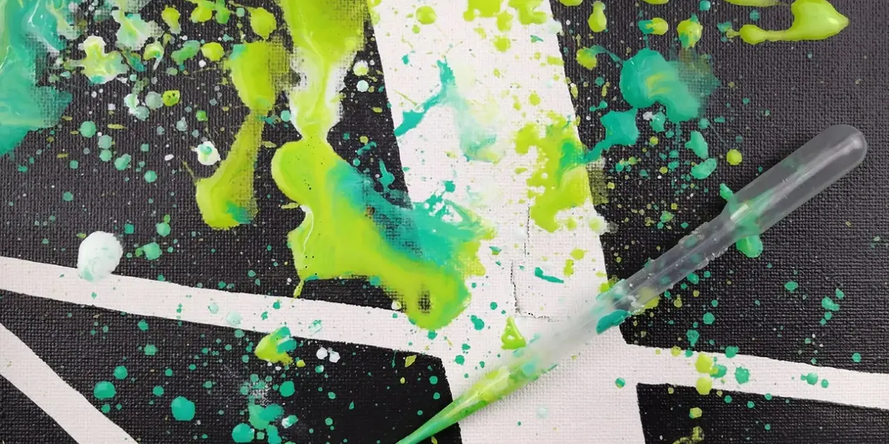 Projection de peinture sur toile, avec des éclaboussures vertes et turquoise sur un fond noir et blanc. Une pipette est visible, prête à projeter plus de peinture.