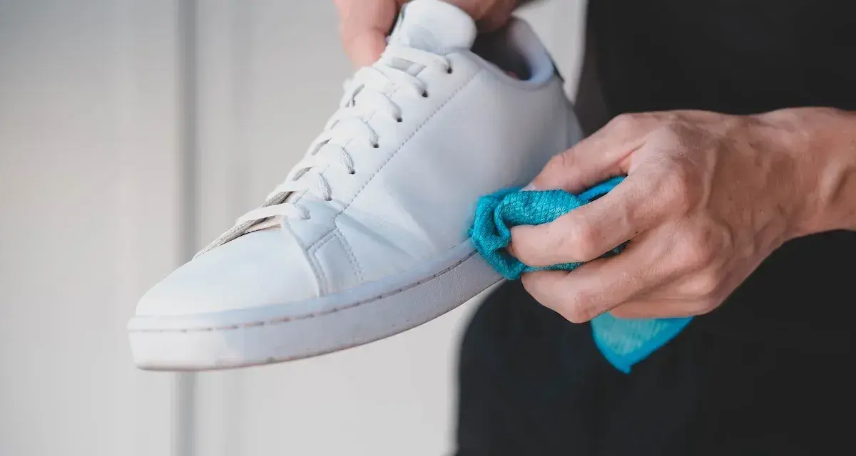 Mani che puliscono una scarpa bianca Adidas Stan Smith con un panno blu. Ecco come lavare le Stan Smith per farle tornare come nuove.