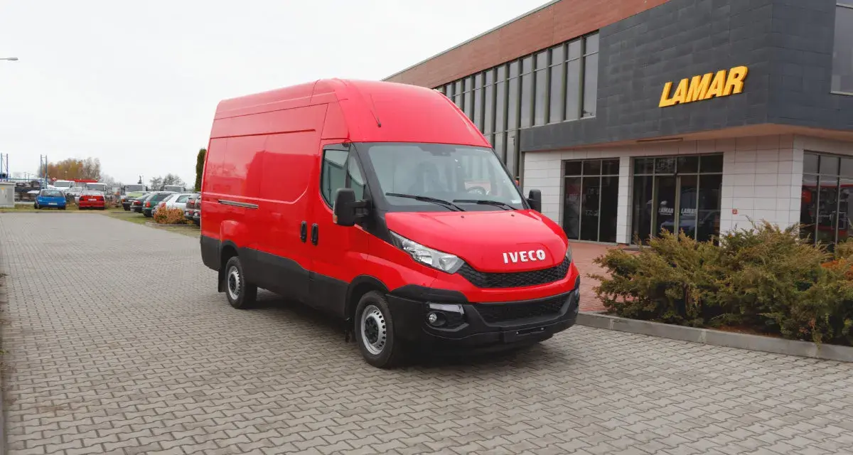 Czerwony bus Iveco na parkingu przed budynkiem z napisem LAMAR.