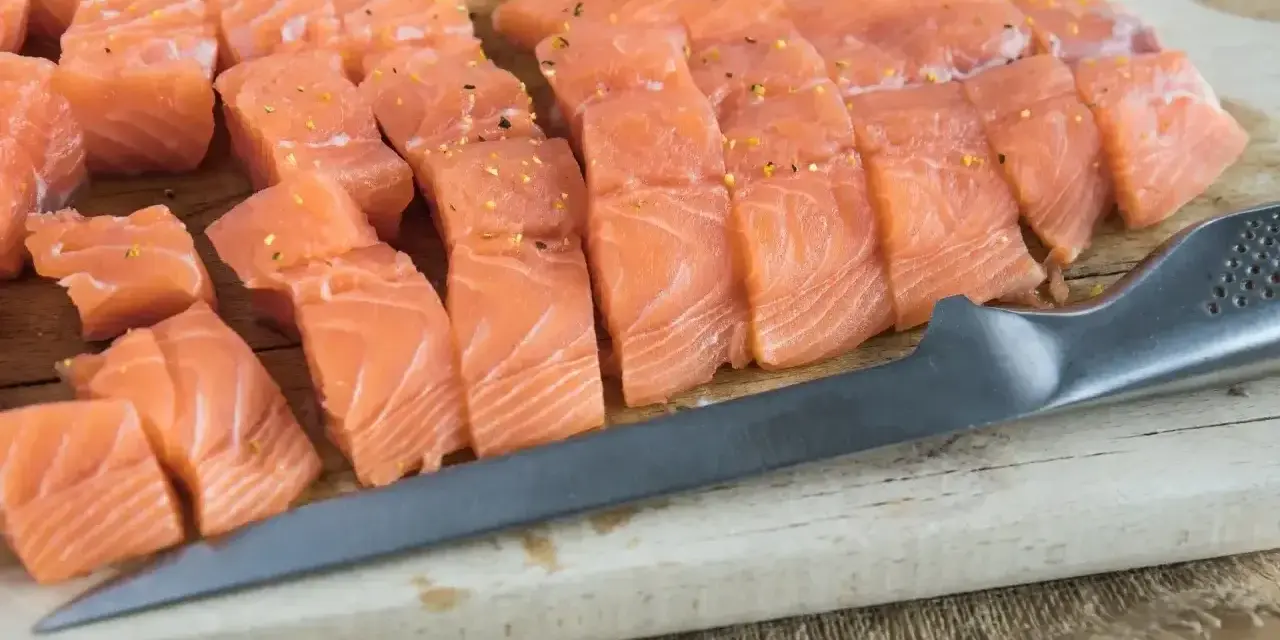 Pokrojony łosoś, idealny jaki łosoś do sushi, leży na desce obok noża.
