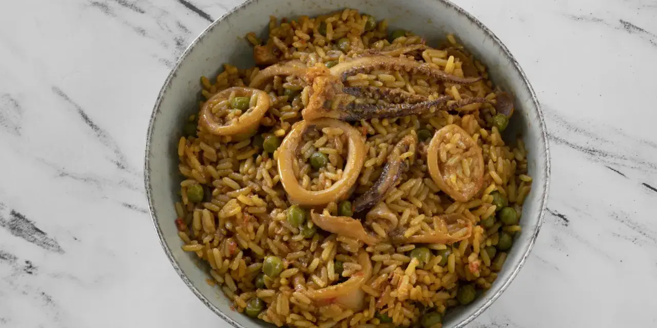 Un delicioso plato de arroz con calamares y guisantes, servido en un cuenco sobre una superficie de mármol.