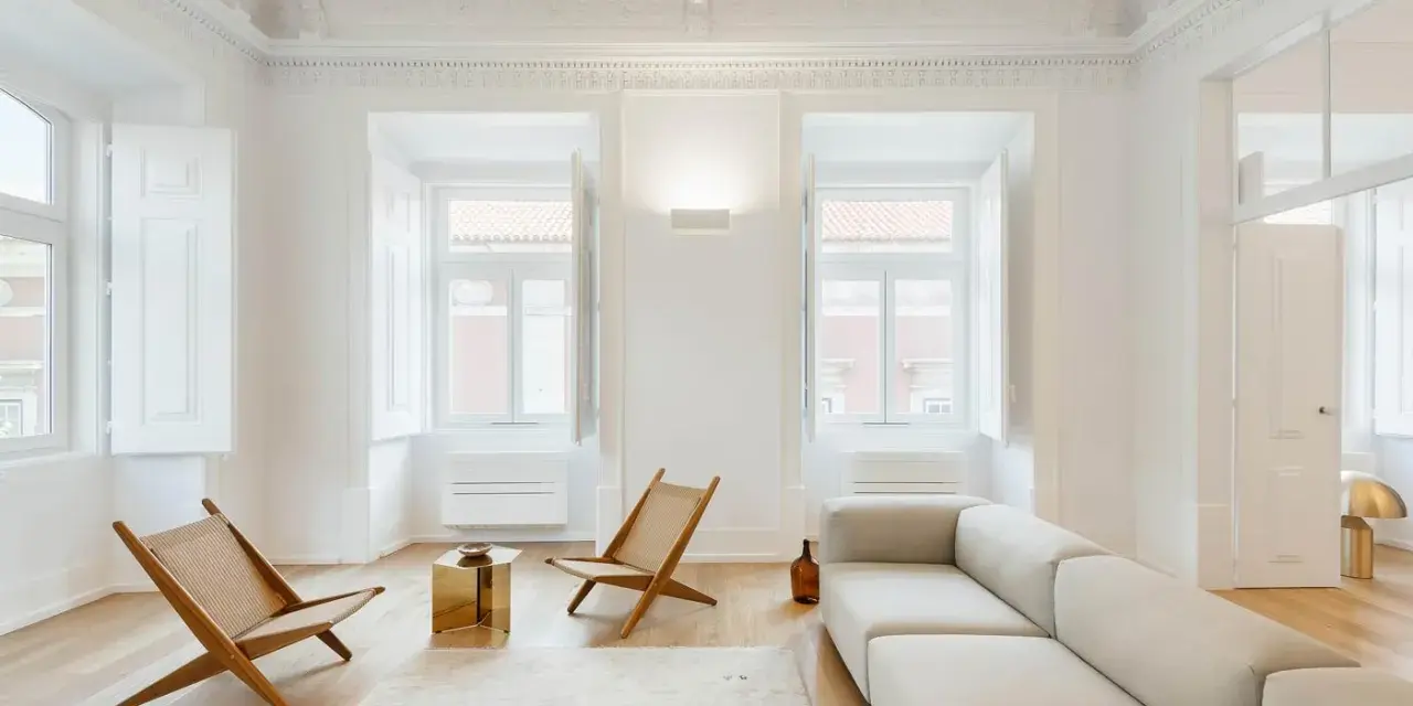 Ecco cosa fa l'architetto d'interni: crea un soggiorno minimalista con divano chiaro, sedie in legno e un tavolino dorato, valorizzando la luce naturale.