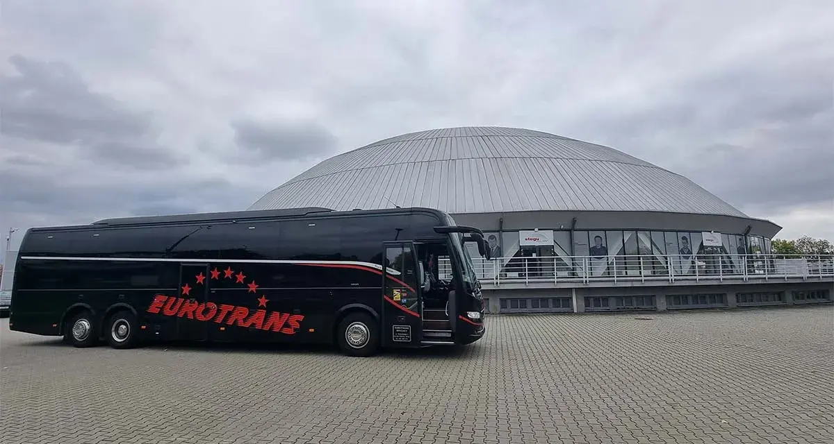 Czarny autokar firmy Eurotrans przed nowoczesnym budynkiem z kopułą.