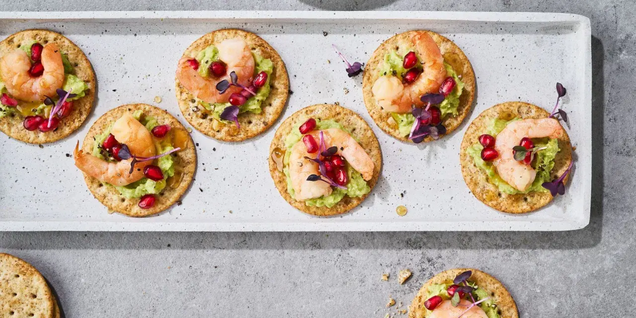 Mediterranes Fingerfood kalt: Garnelen auf Avocado-Creme mit Granatapfelkernen und Kräutern auf Crackern.