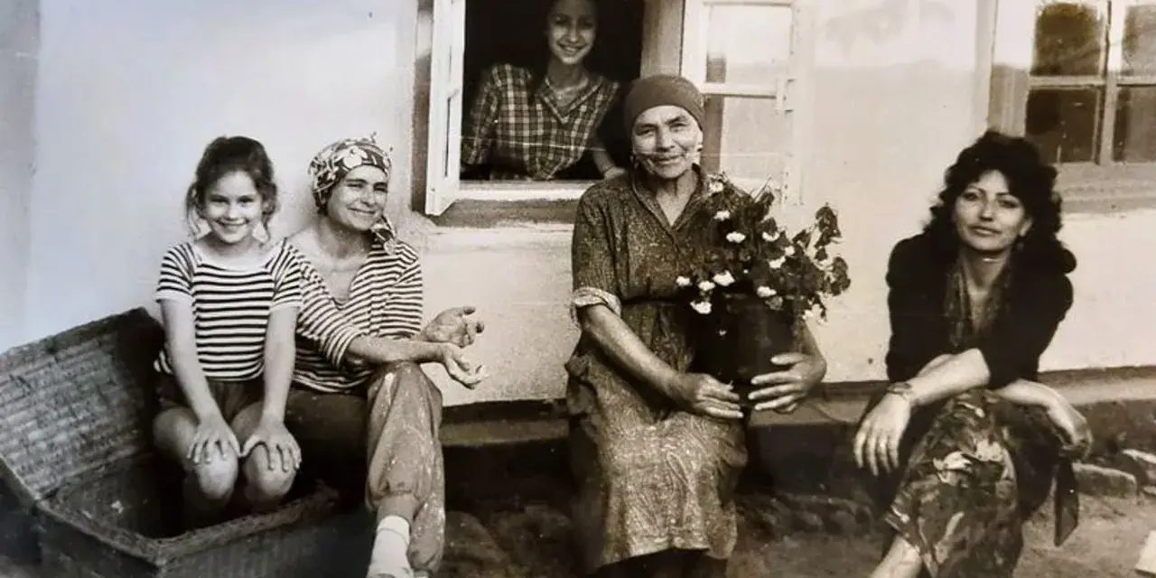 Maria Wojewodzka z rodziną na tle domu. Kobiety w różnym wieku, jedna z nich trzyma kwiaty.