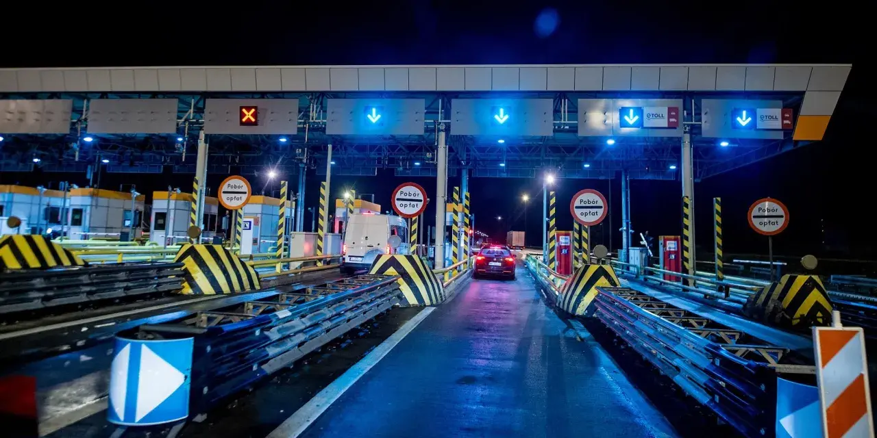 Nocny widok na bramki autostradowe z niebieskimi światłami i znakami, samochody wjeżdżają na płatne pasy.