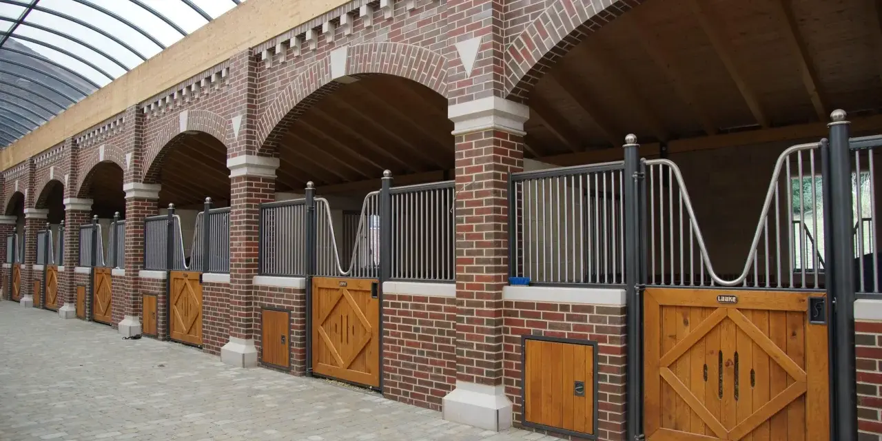 Belle écurie pour chevaux avec des boxes en briques rouges, des portes en bois et un toit transparent.