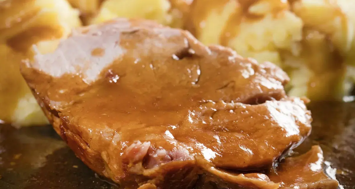 Mięciutka karkówka w sosie, podana z purée ziemniaczanym. Danie wygląda apetycznie i soczyście.