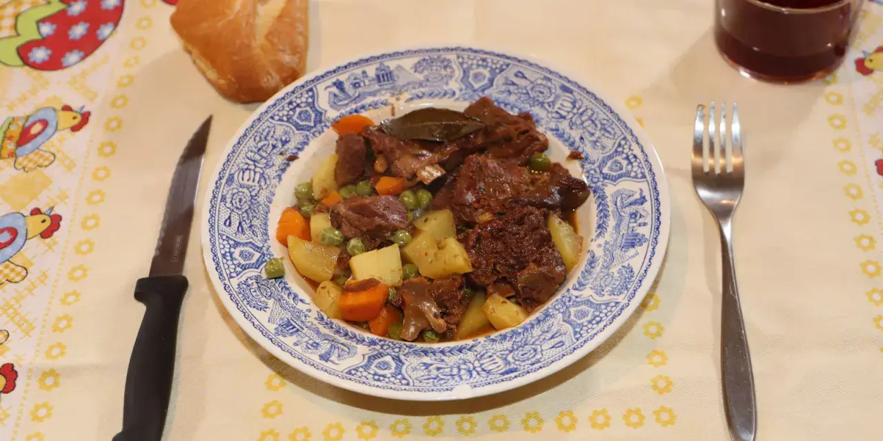 Un plato de corzo guisado con patatas, zanahorias y guisantes, acompañado de pan y vino tinto. ¡Una de las mejores recetas de corzo guisado!
