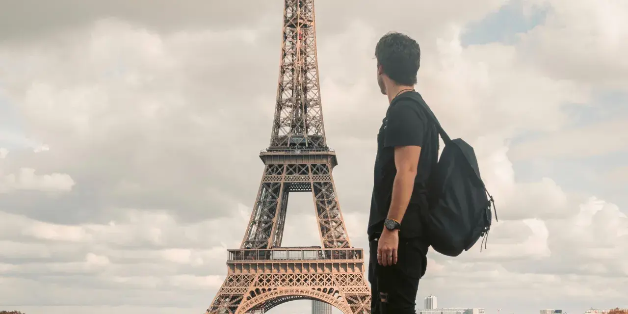 Un joven con mochila admira la Torre Eiffel. Quizás piensa que es dificil aprender francés, pero París es hermoso.
